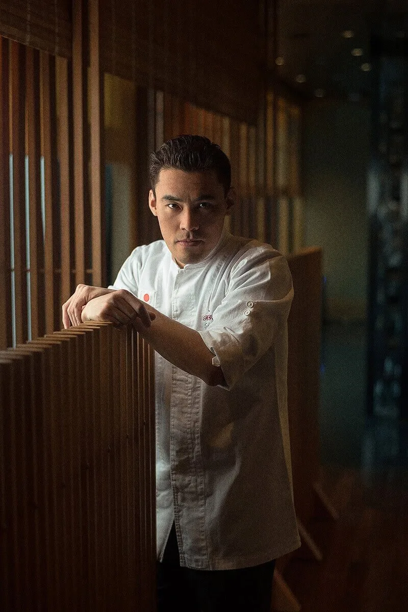 Chef in a white jacket leaning on a wooden screen in a restaurant