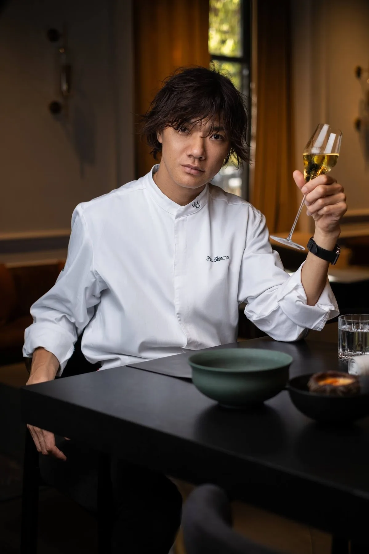 Chef in a white jacket at a table with a glass of wine