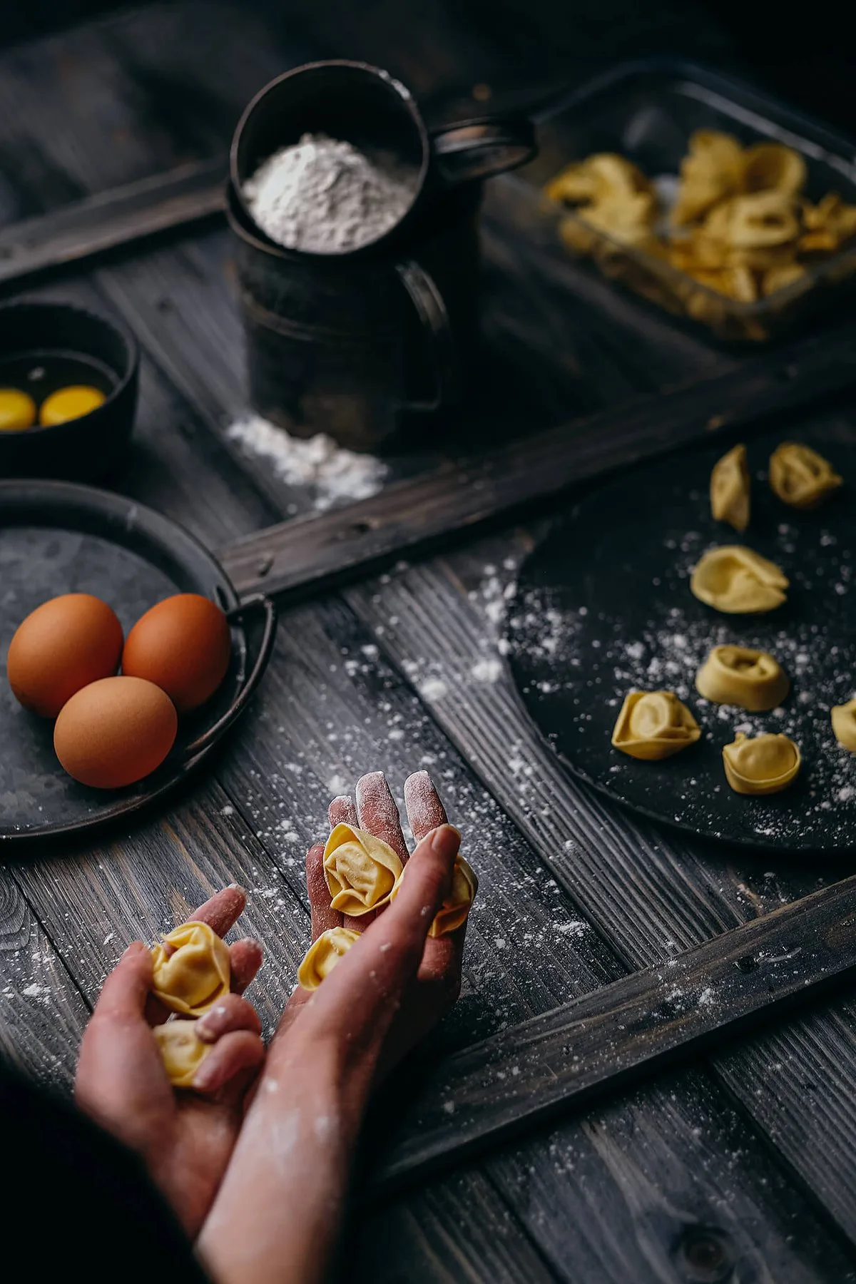 Hands shaping tortellini with flour and eggs, top view