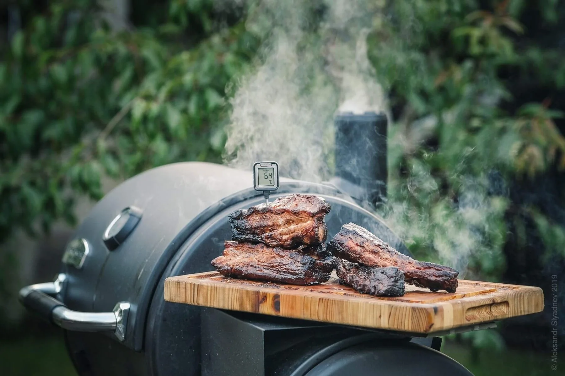 Ribs on a board beside a smoker in the garden